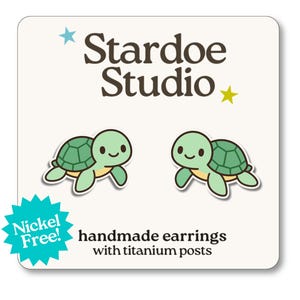 May include: A pair of handmade turtle earrings with titanium posts. The earrings feature a cute cartoon turtle design in shades of green and yellow. The text "Stardoe Studio" is at the top, with "Nickel Free!" in a turquoise burst.