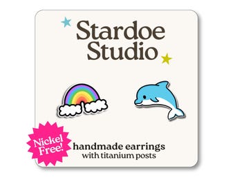 May include: Handmade earrings with titanium posts, featuring a rainbow and a blue dolphin design. The earrings are nickel-free and presented on a cream card with the text "Stardoe Studio".