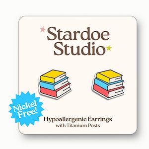 May include: Hypoallergenic earrings with titanium posts, each featuring a stack of three books in yellow, blue, and red. The earrings are presented on a cream card with the text "Stardoe Studio" and "Nickel Free!"