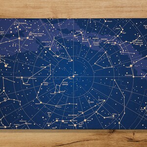 以下が含まれることがあります： 夜空の星座の地図が描かれた青い背景。地図には、北斗七星、小北斗七星、北アメリカ星雲など、星や星座の位置が示されています。地図は白い枠で囲まれています。