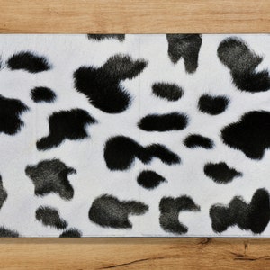 Puede incluir: Una tela con estampado blanco y negro con textura peluda. El patrón se asemeja a una piel de vaca o un estampado dálmata.