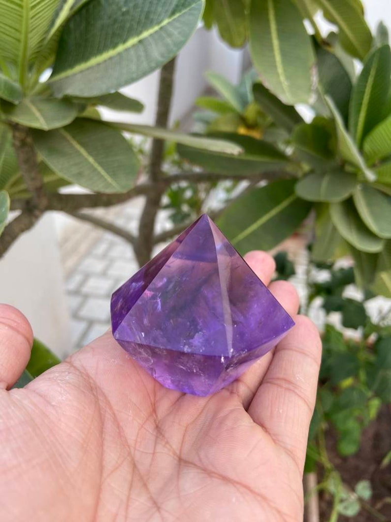 May include: A purple amethyst crystal shaped like a pyramid. The crystal is smooth and polished, with a deep purple color.