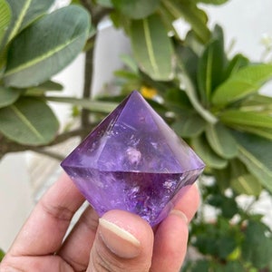 May include: A purple amethyst crystal shaped like a pyramid with a pointed top.