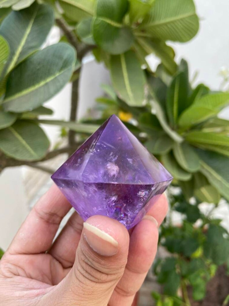 May include: A purple amethyst crystal shaped like a pyramid with a pointed top.