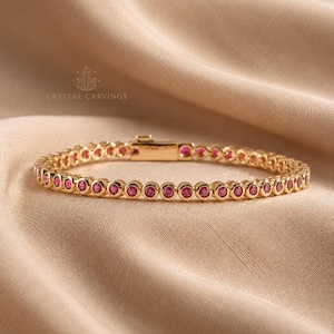 Può includere: Un bracciale tennis color oro caratterizzato da una fila continua di pietre preziose rotonde color rosa vivace, incastonate in castoni circolari individuali. Il bracciale include una chiusura rettangolare sicura e riporta il testo CRYSTAL CARVINGS.