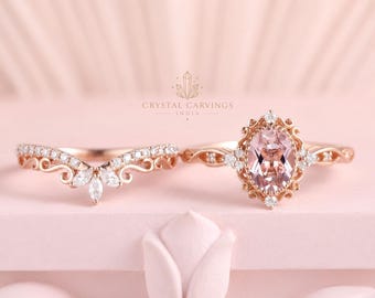 May include: A rose gold ring set featuring an oval-cut peach-coloured centre stone surrounded by a decorative filigree frame with small round diamonds, paired with a matching V-shaped band adorned with marquise and round diamonds. Text: CRYSTAL CARVINGS INDIA.