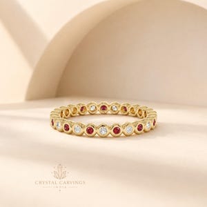 May include: A gold eternity band featuring a repeating pattern of bezel-set round red rubies and clear white diamonds. The ring has a polished metallic finish and a consistent circular design, with the text CRYSTAL CARVINGS INDIA visible below.