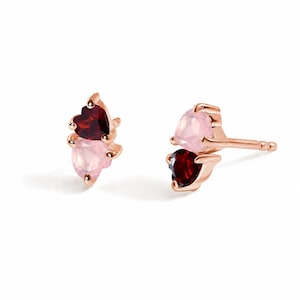 Puede incluir: Un par de pendientes de botón en oro rosa, cada uno con dos piedras preciosas en forma de corazón apiladas verticalmente. Una piedra es un granate rojo oscuro y la otra es un cuarzo rosa pálido. Los pendientes incluyen postes estándar.