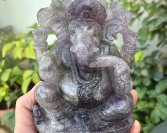 Puede incluir: Estatua de Ganesha de amatista púrpura tallada en una sola pieza de amatista. La estatua está detallada con tallas intrincadas y tiene un acabado liso y pulido.