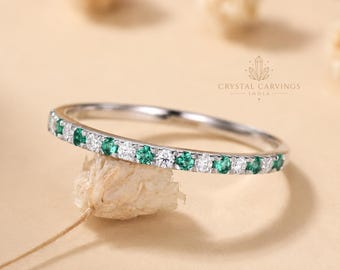 May include: A thin silver-toned band ring featuring an alternating pattern of small, round-cut green emeralds and clear white diamonds. The ring is marked with the text CRYSTAL CARVINGS INDIA. The design is a simple, slender eternity-style band.