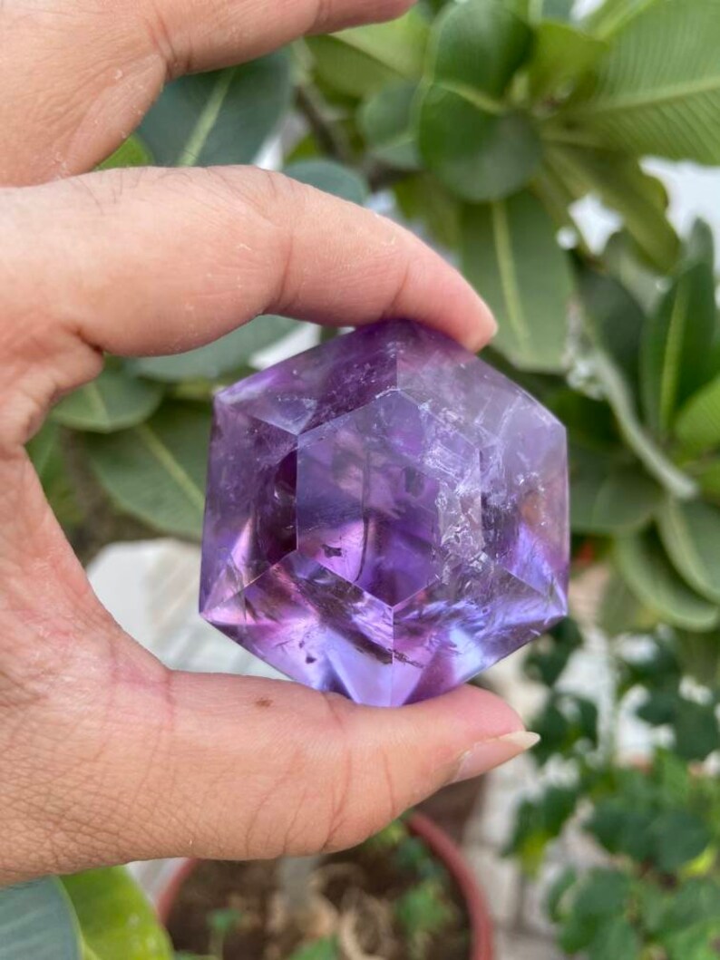 May include: A purple amethyst crystal shaped like a geometric hexagon. The crystal is clear and has a slight shimmer.