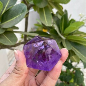 May include: A purple amethyst crystal carved into a geometric shape. The crystal is faceted and has a translucent appearance.