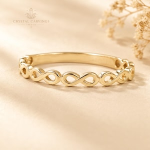 May include: A gold-toned ring featuring a continuous band of repeating infinity symbols. The metal has a polished, reflective surface. The design consists of interconnected loops forming a circular shape, presented with the text Crystal Carvings India.