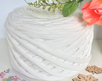 May include: A large white ball of t-shirt yarn, also known as chunky yarn, is shown on a white surface. The yarn is made from recycled t-shirts and is perfect for crafting.