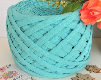 May include: A close-up of a skein of light blue t-shirt yarn. The yarn is woven into a circular shape and is ready to be used for crafting. The yarn is labeled "YarnsGlory" and is described as "Premium T-shirt yarn. Micro-crochet strings. Wooden products for craft."