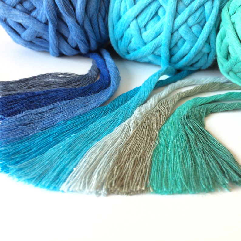 May include: A collection of yarn strands in shades of blue, green, and gray. The yarn is arranged in a gradient pattern, with the darkest blue at one end and the lightest green at the other. The yarn is soft and fluffy, and it would be perfect for knitting or crocheting.