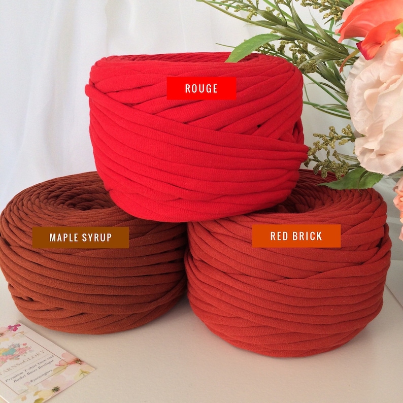 May include: Three balls of yarn in different shades of red. The top ball is labeled "ROUGE", the middle ball is labeled "MAPLE SYRUP", and the bottom ball is labeled "RED BRICK".