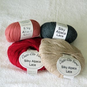 May include: Four skeins of Silky Alpaca Lace yarn in shades of red, pink, gray, and beige. Each skein has a label that reads "Classic Elite Yarns Silky Alpaca Lace". The yarn is displayed on a white, textured surface.