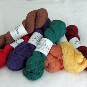 May include: A collection of eight skeins of yarn in various colors including brown, red, purple, dark green, orange, yellow, and burgundy. Each skein features a white paper label with the text JaggerSpun Spinners of Natural Fiber Since 1880.