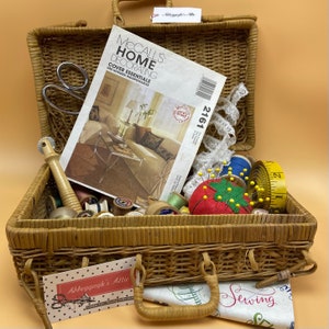 May include: A wicker basket filled with sewing supplies, including spools of thread, buttons, needles, and a McCall's Home Decorating pattern book. The basket has a handle and a label that reads "Abbygayle's Attic".
