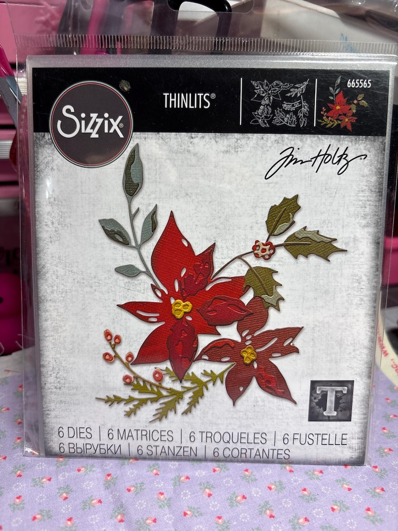 May include: Sizzix Thinlits die set with a poinsettia and holly design. The package contains 6 dies, 6 matrices, and other die-cutting tools. The image shows a red poinsettia flower with green leaves and berries, ideal for paper crafting projects.