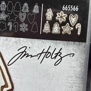 Puede incluir: Un juego de troqueles en blanco y negro con varias formas tem&aacute;ticas navide&ntilde;as, incluyendo casas de jengibre, estrellas y &aacute;rboles de Navidad. El n&uacute;mero 665566 est&aacute; impreso en blanco. Tambi&eacute;n se ve la firma "Tim Holtz".