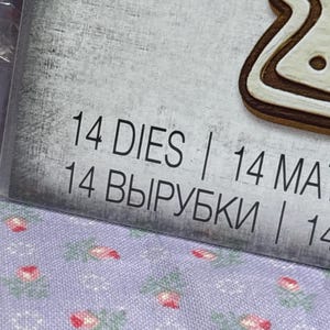 Puede incluir: Primer plano de un paquete con el texto "14 DIES" y "14 MAT". El fondo es una superficie gris claro texturizada. Se ve un troquel con forma de galleta de jengibre. La parte inferior de la imagen muestra una tela con estampado floral.