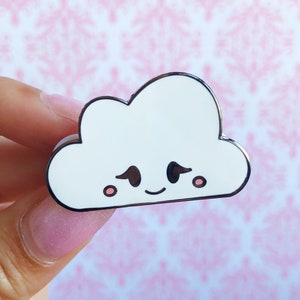 以下が含まれることがあります： 笑顔と赤いほっぺたをした雲の形をした白いエナメルピン。雲は黒い目と黒い口をしています。