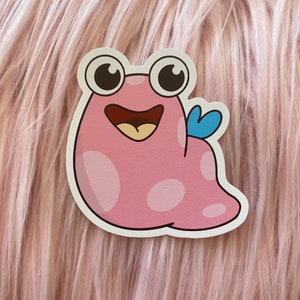 May include: A pink cartoon character with large eyes and a wide smile. The character has a blue wing and white spots.