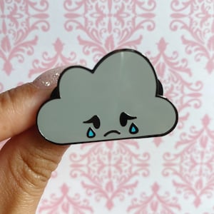 May include: A grey cloud shaped enamel pin with a sad face and blue teardrop details.