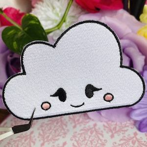 May include: White cloud shaped embroidered patch with a black outline and a cute cartoon face with black eyes, pink cheeks, and a smiling mouth.