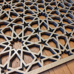 K&ouml;nnte beinhalten: Eine dekorative Holz-Wandverkleidung mit einem geometrischen Muster aus &uuml;berlappenden Sternen. Die Verkleidung ist aus hellbraunem Holz gefertigt und hat eine silberne Oberfl&auml;che.