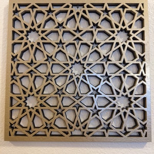 K&ouml;nnte beinhalten: Eine goldene Wanddekoration aus Metall mit einem geometrischen Muster aus Sternen und filigranen Linien. Das Design erinnert an islamische Architektur.
