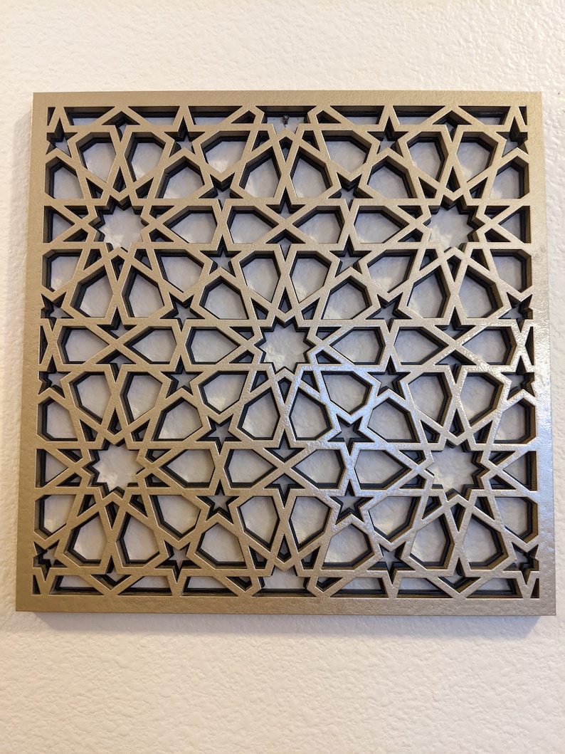 K&ouml;nnte beinhalten: Eine goldene Wanddekoration aus Metall mit einem geometrischen Muster aus Sternen und filigranen Linien. Das Design erinnert an islamische Architektur.