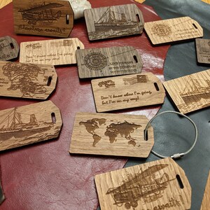 May include: A collection of wooden luggage tags with various designs and sayings. The tags feature images of airplanes, ships, maps, and compasses. Some of the sayings include "Adventure awaits!" and "Not all who wander are lost".