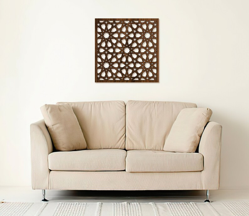 K&ouml;nnte beinhalten: Eine braune Holz-Wanddekoration mit geometrischem Muster. Die Dekoration h&auml;ngt an einer wei&szlig;en Wand &uuml;ber einem beigen Sofa.