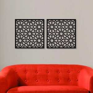 K&ouml;nnte beinhalten: Zwei schwarze Wanddekorationspaneele aus Metall mit einem geometrischen Muster aus Sternen und Kreisen. Die Paneele h&auml;ngen an einer wei&szlig;en Wand &uuml;ber einem roten Sofa.