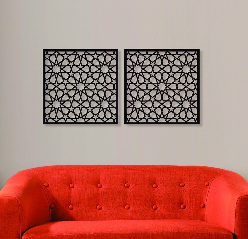 K&ouml;nnte beinhalten: Zwei schwarze Wanddekorationspaneele aus Metall mit einem geometrischen Muster aus Sternen und Kreisen. Die Paneele h&auml;ngen an einer wei&szlig;en Wand &uuml;ber einem roten Sofa.