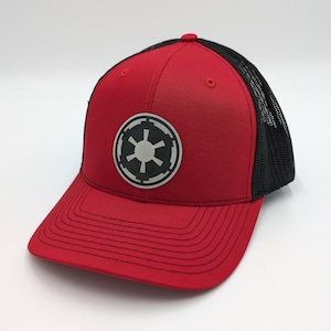 May include: A red and black trucker hat with a black and white Imperial symbol patch on the front.