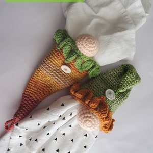 May include: Two crocheted gnome ornaments with a white towel with black triangle pattern. One gnome is orange and green, the other is brown and green. Both have white button eyes and pink noses.