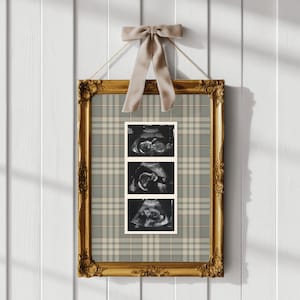 May include: A rectangular gold ornate frame containing a vertical strip of three black and white ultrasound images set against a beige and grey plaid background. A light beige ribbon is tied in a bow at the top of the frame for hanging.