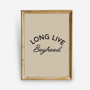 Puede incluir: Una impresión enmarcada con un marco dorado y un fondo beige. La impresión presenta el texto "LONG LIVE Boyhood" en negro.
