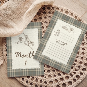 May include: Two rectangular cards with a sage green and tan plaid border and a textured white center. One card features a brown illustration of a person riding a bucking horse and the text Month 1. The other card shows a cowboy hat illustration with lines for date, weight, height, and sweet moments this month.