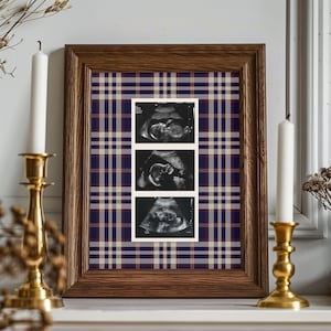 May include: A rectangular wooden frame containing a vertical strip of three black and white ultrasound images set against a background with a navy blue, red, and beige plaid pattern. The frame is positioned between two brass candle holders.