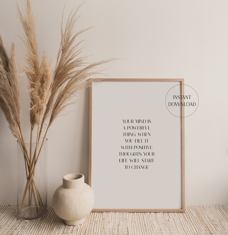 Pode incluir: Uma impress&atilde;o de arte de parede imprim&iacute;vel com uma cita&ccedil;&atilde;o motivacional: "Sua mente &eacute; uma coisa poderosa quando voc&ecirc; a enche de pensamentos positivos, sua vida come&ccedil;ar&aacute; a mudar." A impress&atilde;o &eacute; emoldurada em uma moldura de madeira clara e &eacute; exibida em uma mesa com um vaso de grama de pampas seca.