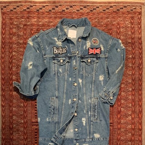 May include: A light blue denim jacket with distressed details and patches. The patches include "The Beatles" and a Union Jack flag.