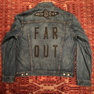 May include: A blue denim jacket with a black embroidered design of a solar system on the back. The text "FAR OUT" is also embroidered on the back in black.