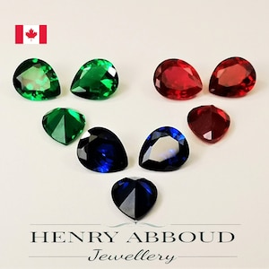 May include: Assortment of pear-shaped gemstones in various colours, including green, red, and blue. The gemstones are arranged in a heart shape on a white surface.  HENRY ABBOUD Jewellery.