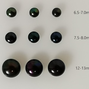 May include: A selection of dark, lustrous pearls in different sizes, from 6.5mm to 13mm. The pearls are arranged in rows, displaying their round shape and iridescent sheen. The image includes the Canadian flag.