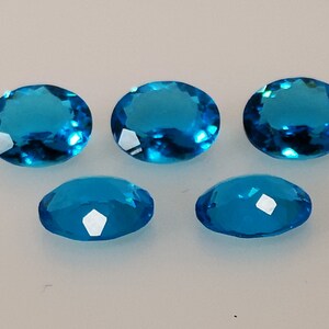 May include: Six oval-shaped, faceted, blue gemstones. The gemstones are translucent and have a light blue colour.